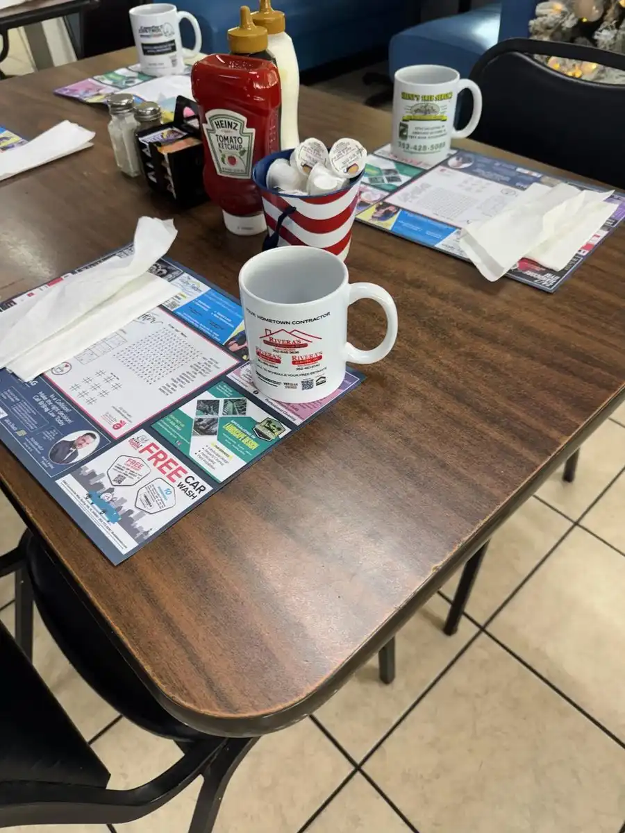 Restaurant table set with advertising placemats, branded coffee mugs, and condiments featuring local business ads