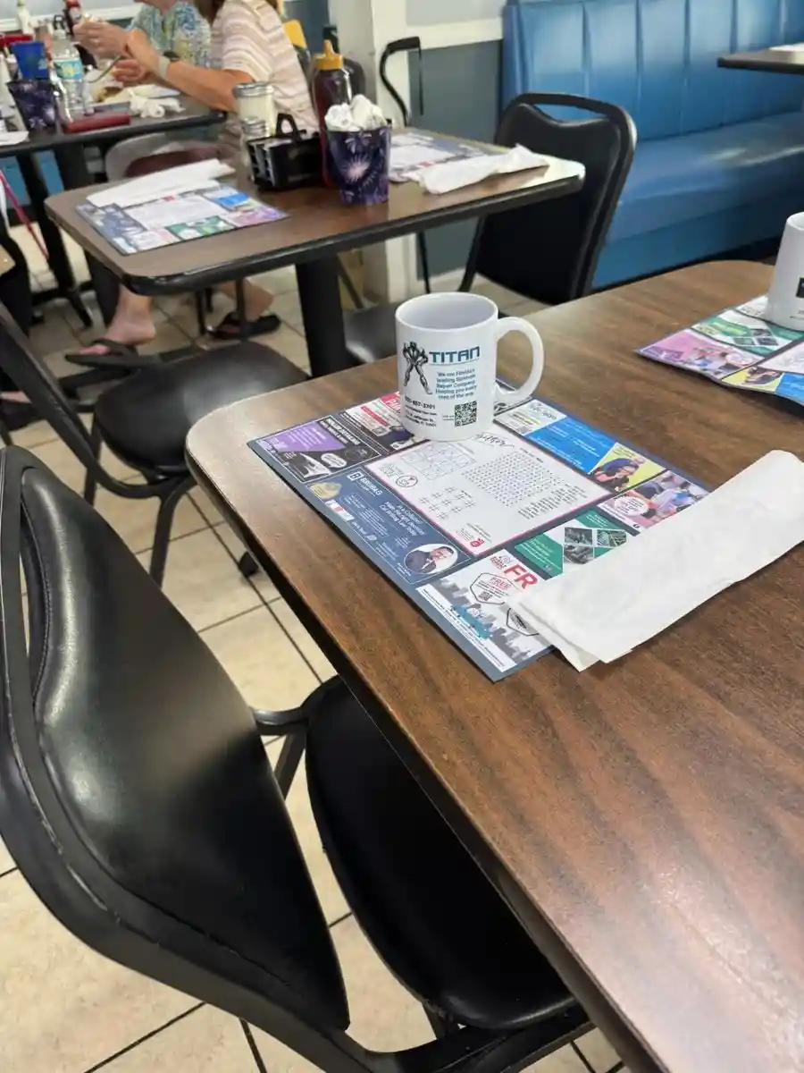 Diner table with a Be Seen Pro advertising placemat, word search puzzle, and TITAN branded coffee mug
