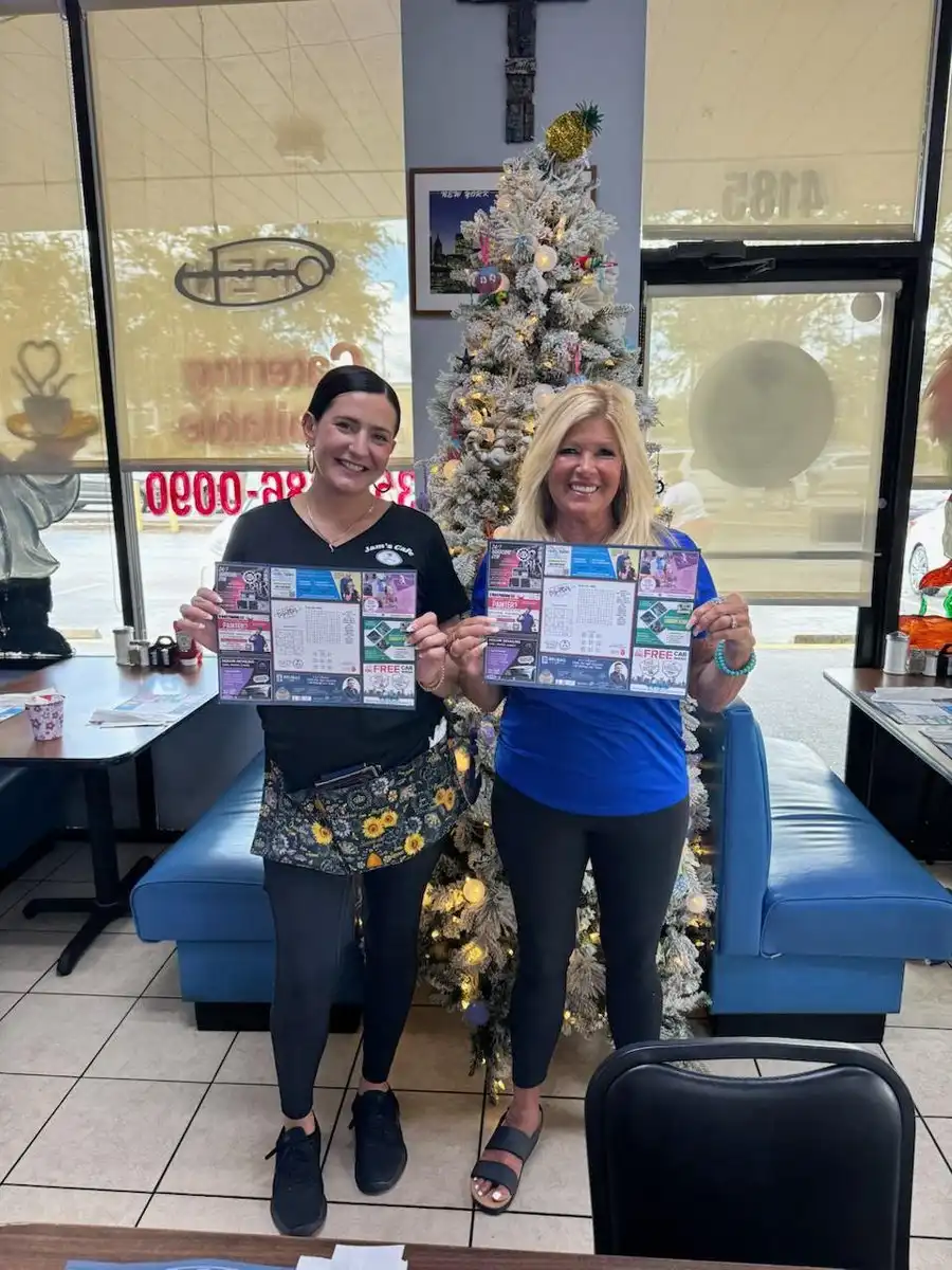 Two women at Jams Cafe holding up Be Seen Pro advertising placemats with local business ads and a word puzzle